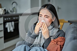 Portrait of ill young korean woman feeling sick, sneezing and holding napkin, staying at home ill, caught cold