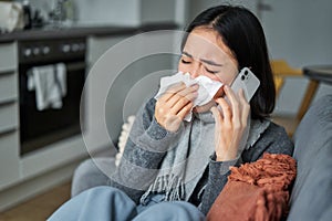 Portrait of ill young korean woman feeling sick, sneezing and holding napkin, staying at home ill, caught cold. Talking