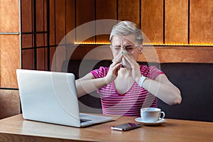 Portrait of illness young bussinesswoman with short blonde hair in pink t-shirt and eyeglasses sitting in cafe and holding napkin