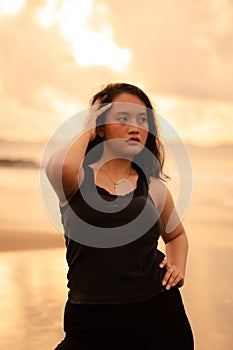 portrait image of an Asian woman with black hair and an angry expression standing on the beach in her black clothes