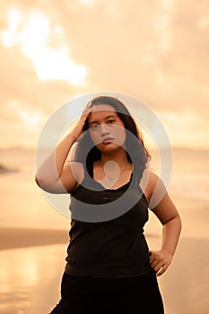 portrait image of an Asian woman with black hair and an angry expression standing on the beach in her black clothes