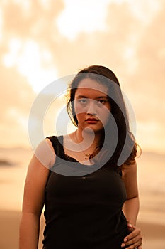 portrait image of an Asian woman with black hair and an angry expression standing on the beach in her black clothes