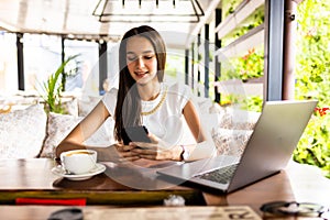 Portrait image of a young woman holding and using mobile phone and laptop in cafe