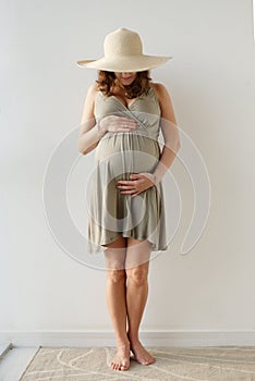 Portrait of the impersonal pregnant woman in the hat holding her big tummy. Waiting for the baby. Motherhood.