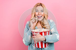Portrait of impressed person with curly hair wear blue cardigan eat popcorn watch intersting movie isolated on pink
