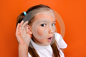 Portrait of impressed schoolkid arm near ear open mouth listen eavesdrop isolated on orange color background