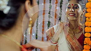 Portrait of an Indian Bengali lady in a red-bordered saree applying bindi on her forehead