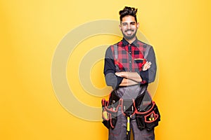 Portrait of indian happy handyman with tool belt isolated on yellow background