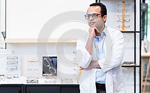 Portrait of Indian middle aged ophthalmologist or optometrist man work at optometry clinic, thinking and standing in front of new