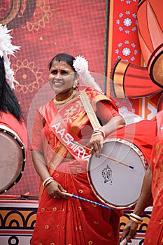 Portrait of an Indian woman wearing a traditional Bengali outfit and playing Dhak Dhol at a puja pandal on the last day of Durga