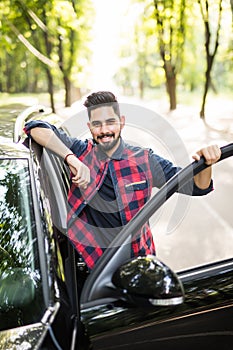 Portrait of a indian young handsome man getting into his car and smiling