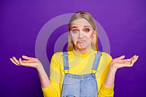 Portrait of indifferent person shrugging her shoulders wearing yellow turtleneck denim jeans overalls isolated purple