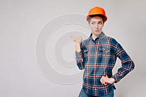 Portrait of an indignant builder`s girl pointing her finger to the side against a light background