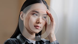 Portrait indoors asian girl millennial woman difficult thoughts thinking solves problem rubs forehead with hand feels