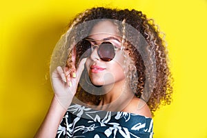 Portrait indoors of a young afro american woman in sunglasses. Yellow background. Lifestyle. Casual clothing