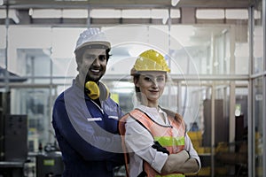 Portrait of industrial engineer worker woman and man wearing helmet standing with arms crossed at manufacturing plant, young