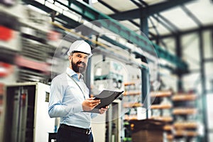 A portrait of an industrial man engineer with clipboard standing in a factory.