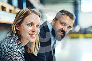 A portrait of an industrial man and woman engineer in a factory, looking at camera.