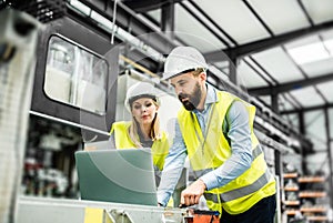 A portrait of an industrial man and woman engineer with laptop in a factory, working.