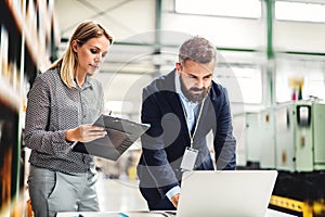 A portrait of an industrial man and woman engineer with laptop in a factory, working.