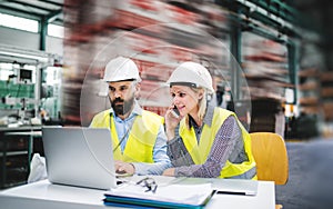 A portrait of an industrial man and woman engineer with laptop in a factory, working.