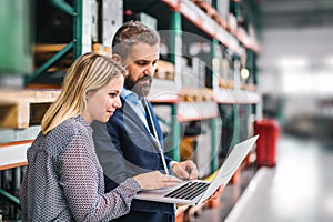 A portrait of an industrial man and woman engineer with laptop in a factory, working.