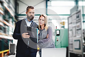 A portrait of an industrial man and woman engineer with laptop in a factory, working.