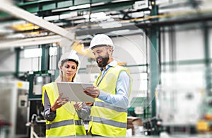 A portrait of an industrial man and woman engineer with tablet in a factory, talking.