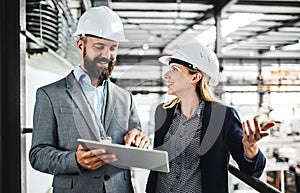 A portrait of an industrial man and woman engineer with tablet in a factory, working.