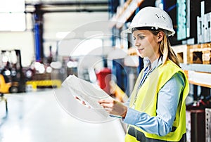 A portrait of an industrial woman engineer in a factory holding paperwork.