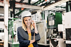 A portrait of an industrial woman engineer on the phone, standing in a factory.