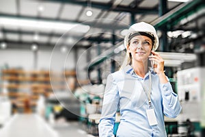 A portrait of an industrial woman engineer standing in a factory, making a phone call.