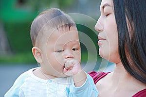 Portrait of infant baby boy is sucking hand with Asian mother carrying