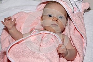 Portrait of Infant baby girl under the pink towel roll looking at camera lying on bed after bath