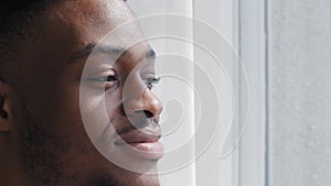 Portrait inspired happy african man feeling harmony looking out window standing at home dreaming thinking about future