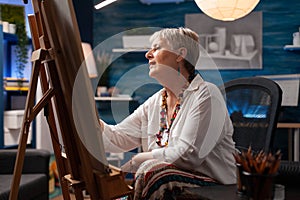 Portrait of inspired retired artist in front of easel drawing creative art masterpiece using pencil