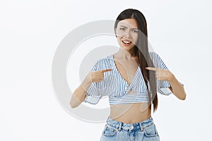 Portrait of insulted and shocked asian woman with dark hair in cropped blouse pointing at herself with index photo