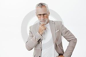 Portrait of intelligent wealthy and thoughtful attractive mature businessman with grey hair rubbing beard looking down