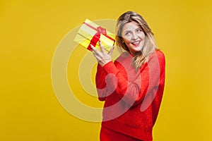 Portrait of interested beautiful blonde woman with red lipstick in bright casual sweater, isolated on yellow background