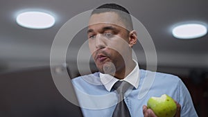 Portrait of interested young African American man eating apple shaking head yes listening to colleague in video chat