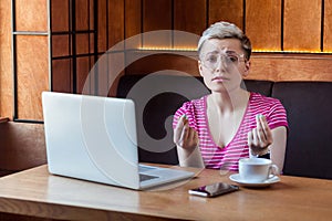 Portrait of interesting sad young freelancer in pink t-shirt is sitting in cafe and agrees with his employer for payment and