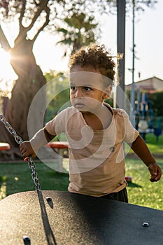 portrait of interracial ethiopian israeli toddler playing in the park at sunset. backlit light rim. olive tree in the background.