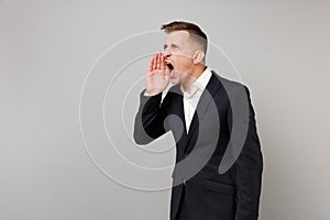 Portrait of irritated young business man in classic black suit, shirt screaming with hand gesture isolated on grey