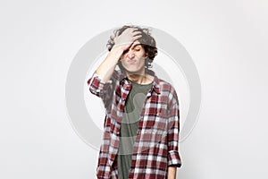 Portrait of irritated young man in casual clothes keeping eyes closed, putting hand on head isolated on white wall