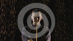 Portrait of a Japanese kendo fighter lowering his shinai towards the camera. Shot on a black background in the rain