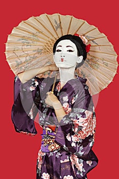 Portrait of Japanese woman in kimono holding parasol against red background
