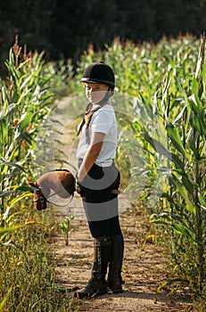 Portrait of a jockey girl in a helmet and a white t-shirt, who sits on a brown toy horse in a corn field photo