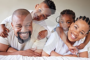 Portrait of a joyful african american family lying on each other on a bed in a bedroom. Black parents spending quality