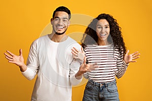 Portrait Of Joyful Arab Couple Spreading Hands With Excitement Over Yellow Background