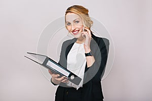 Portrait joyful blonde businesswoman talking on phone, holding folder, smiling to camera isolated on white background